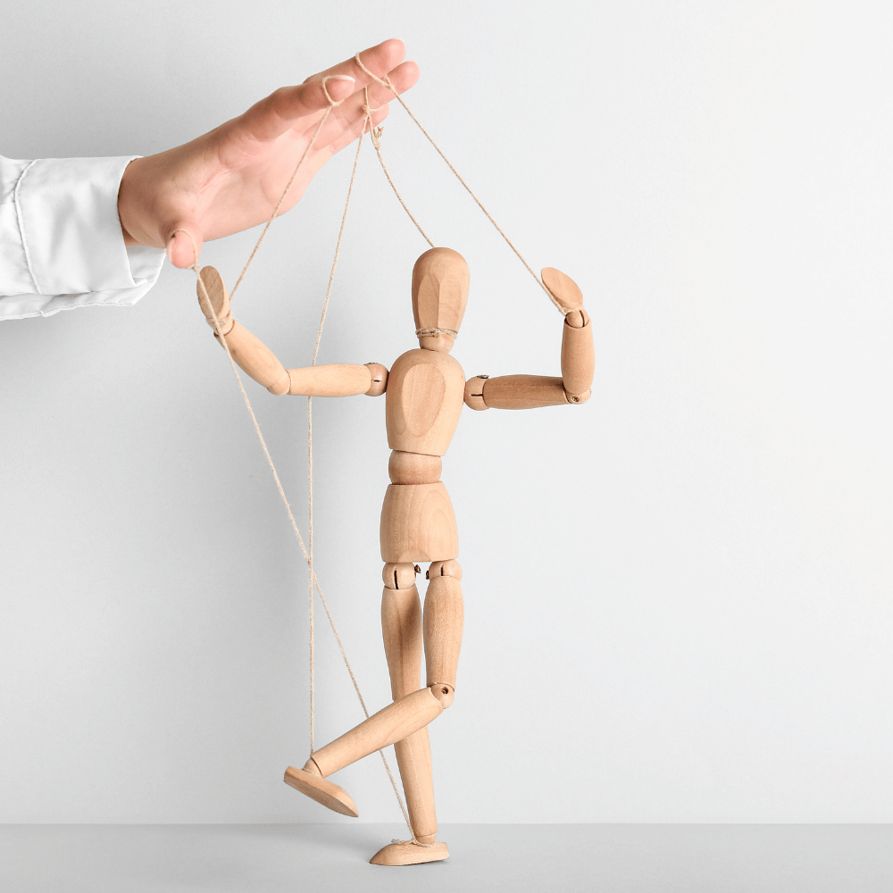 Eine Holzfigur, die mit Seilen von einer Hand gesteuert wird.